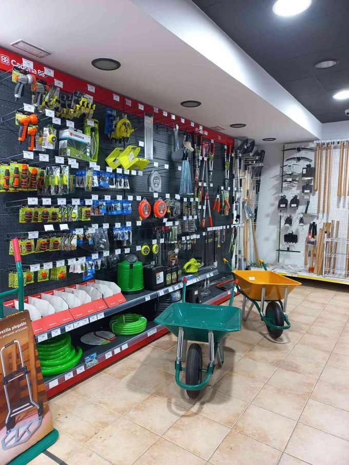 Interior de una ferretería con herramientas y artículos de jardinería en estantes y tableros perforados. 