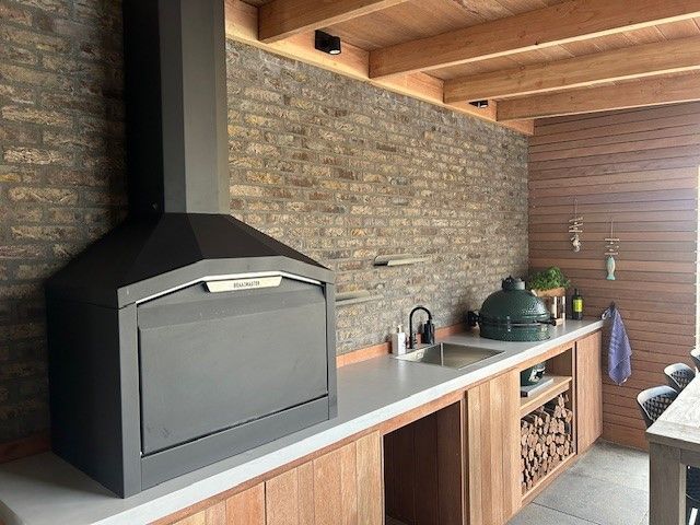 Braaimaster: Cuisine extérieure avec barbecue au charbon de bois, évier et placards en bois.