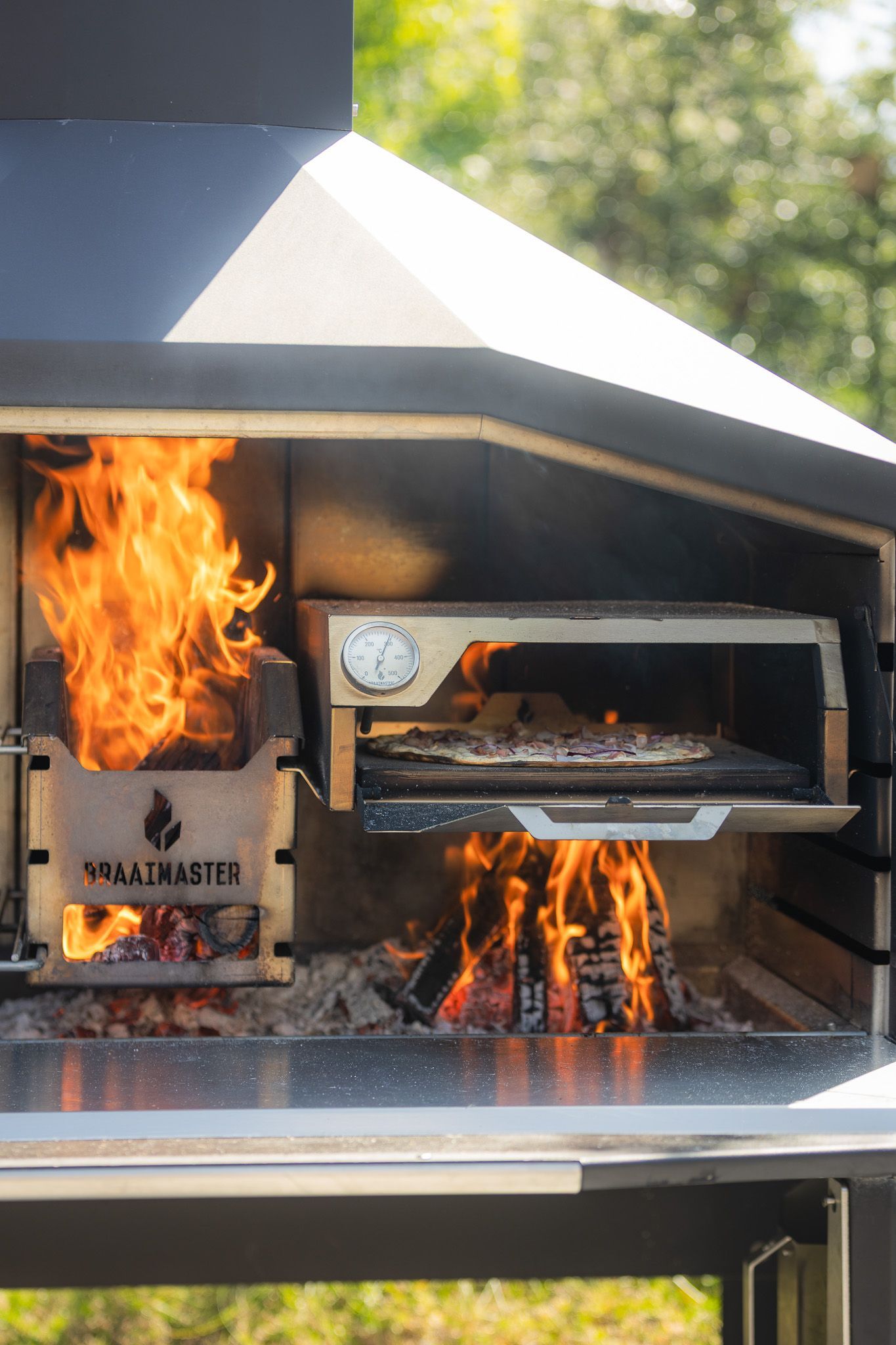 Braaimaster: Four à pizza au feu de bois avec flammes, pizzas à l'intérieur et à l'extérieur. 