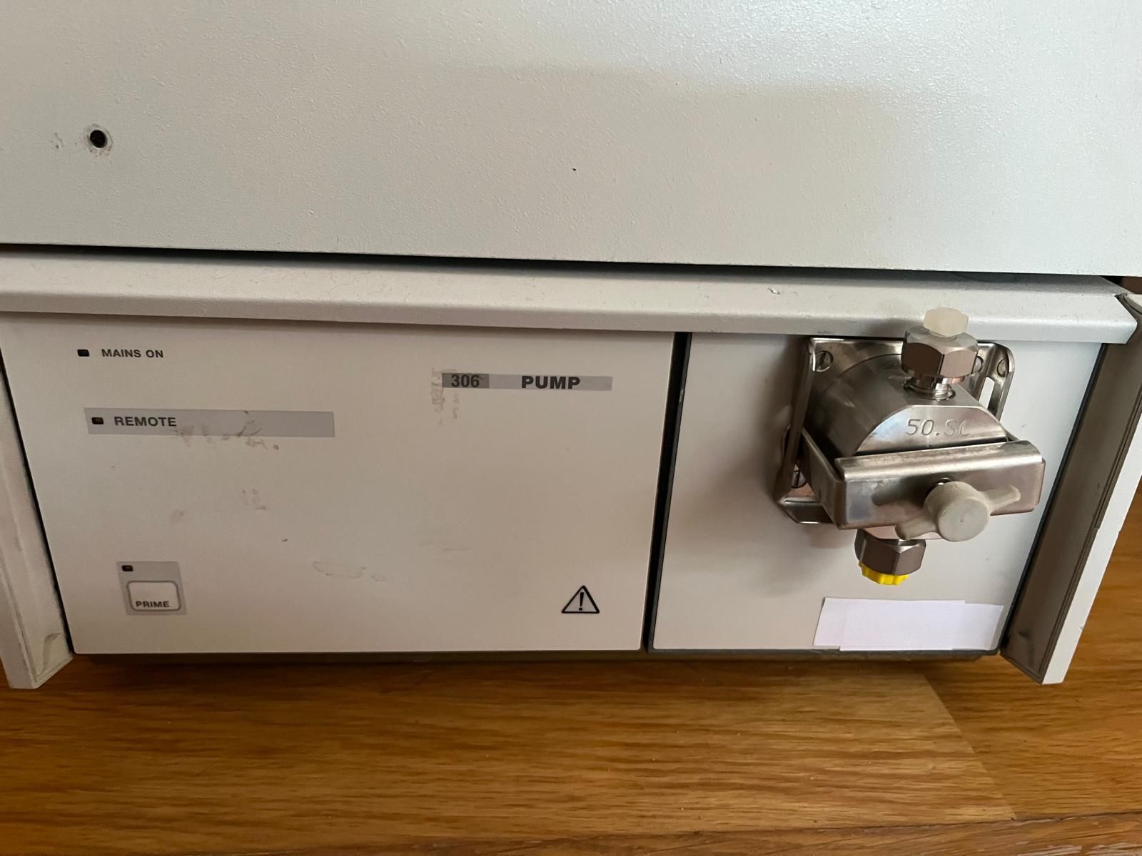 Primer plano de un instrumento HPLC blanco que muestra una bomba y etiquetas asociadas, con una superficie de madera debajo.