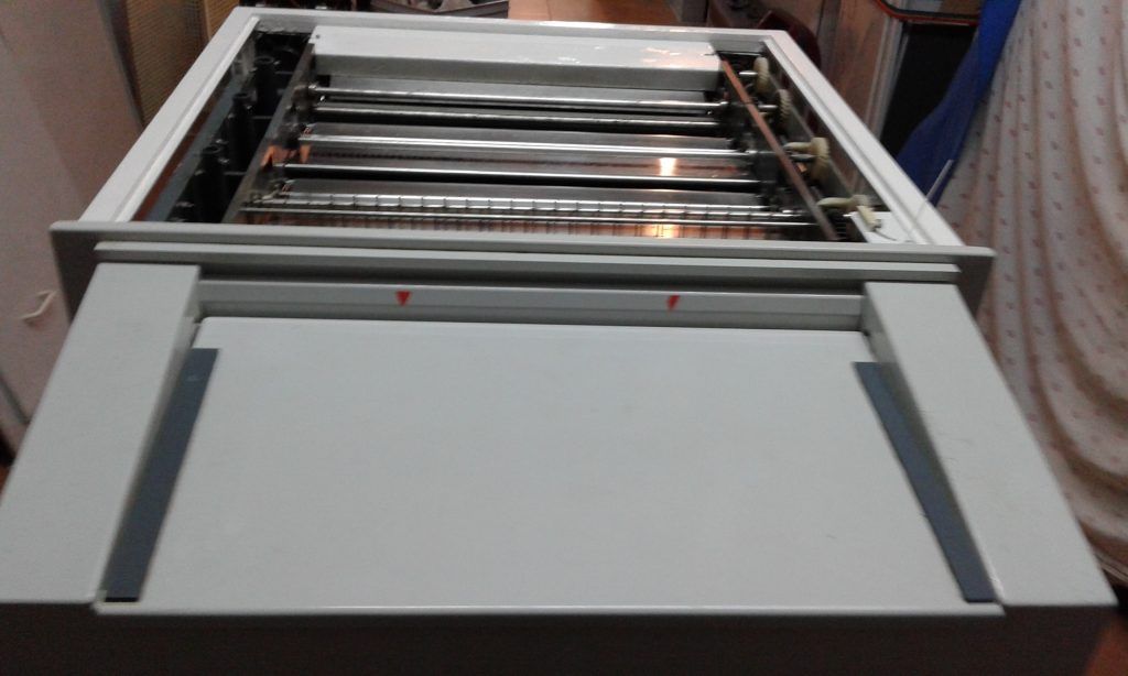 Máquina blanca con parte superior abierta que revela rodillos metálicos y bandeja extraíble.