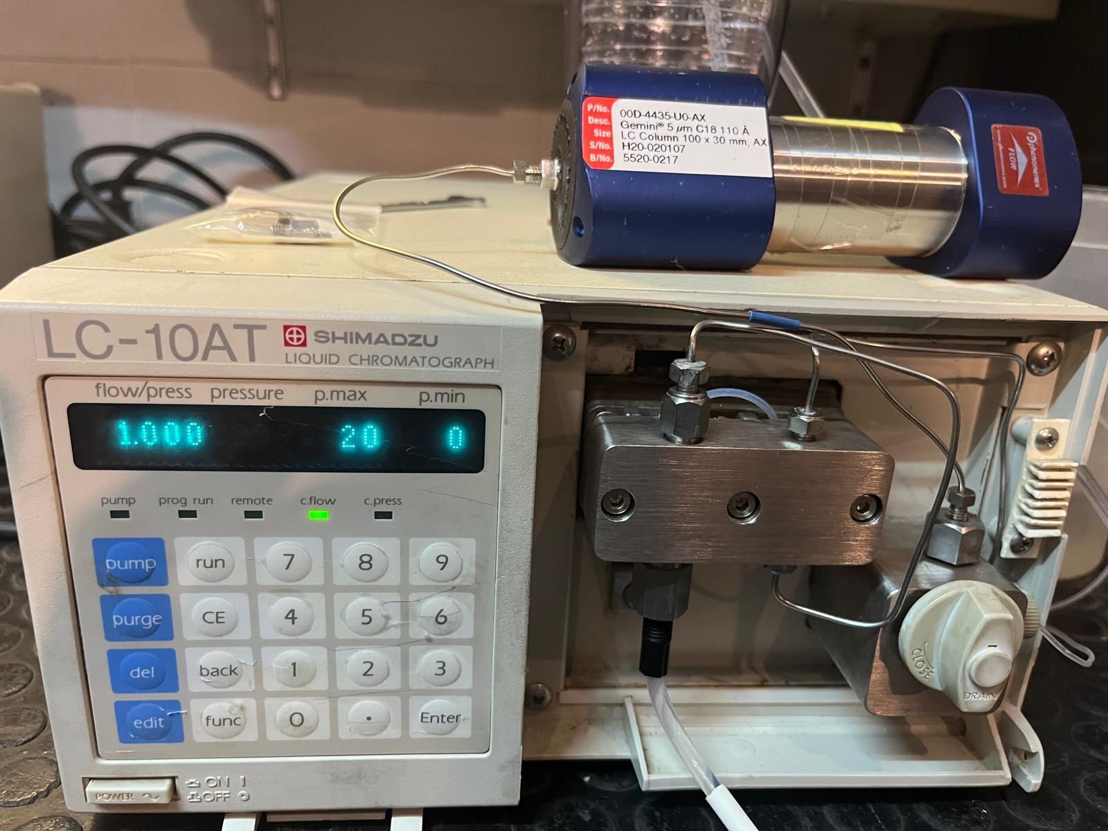 Máquina HPLC LC-10AT con cabezal de bomba azul. La pantalla muestra el caudal y otros ajustes.