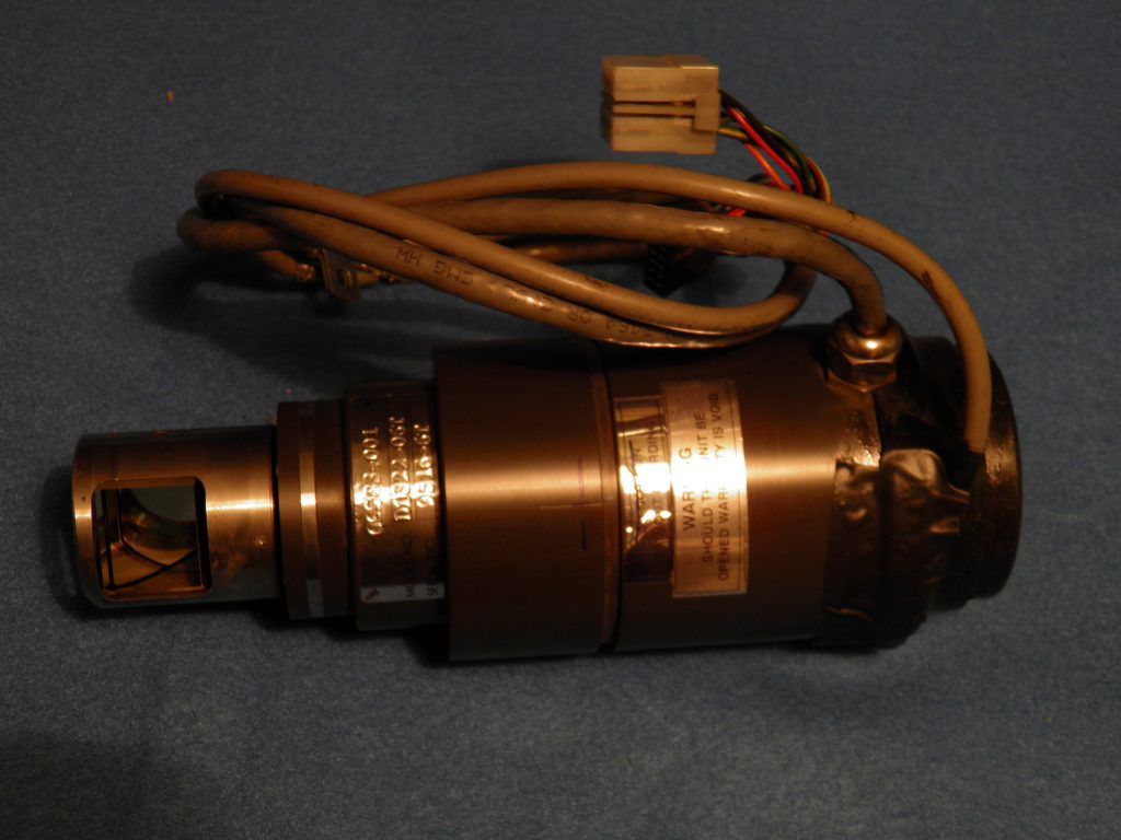 Instrumento cilíndrico oscuro con extremo cuadrado y cableado adjunto.