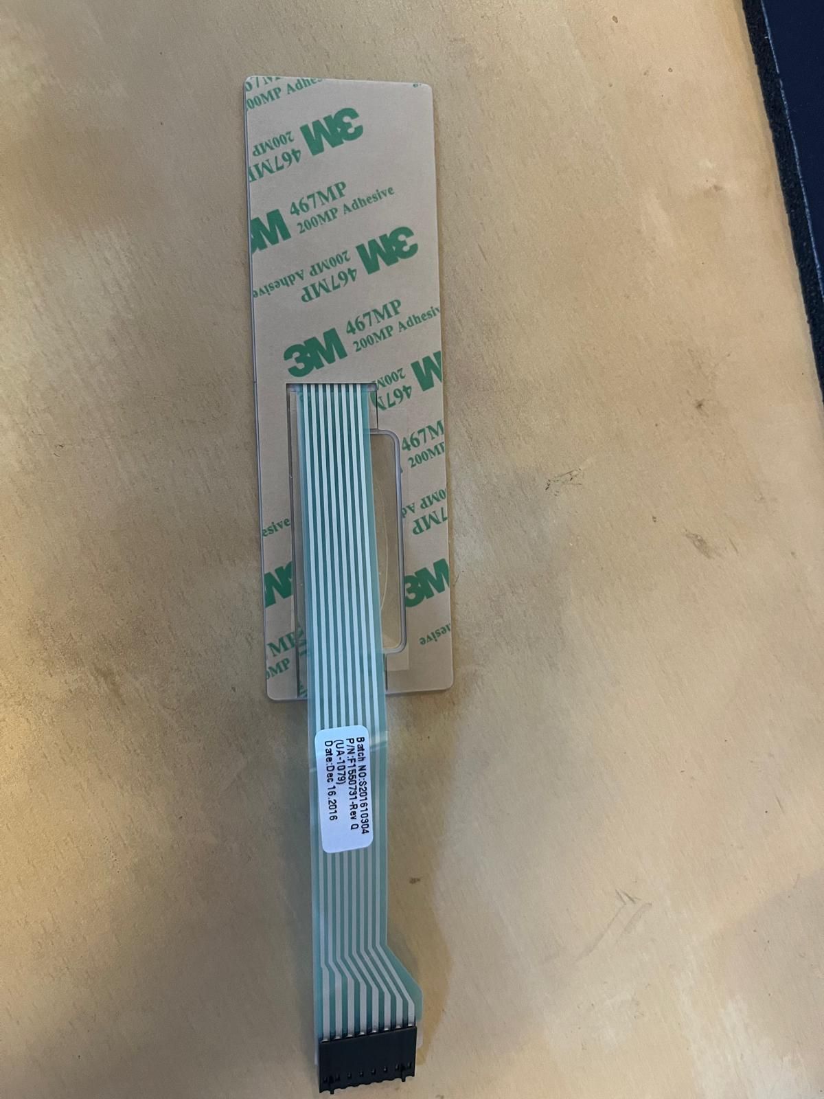 Cable de circuito flexible con conector negro y fijado a una lámina adhesiva 3M.