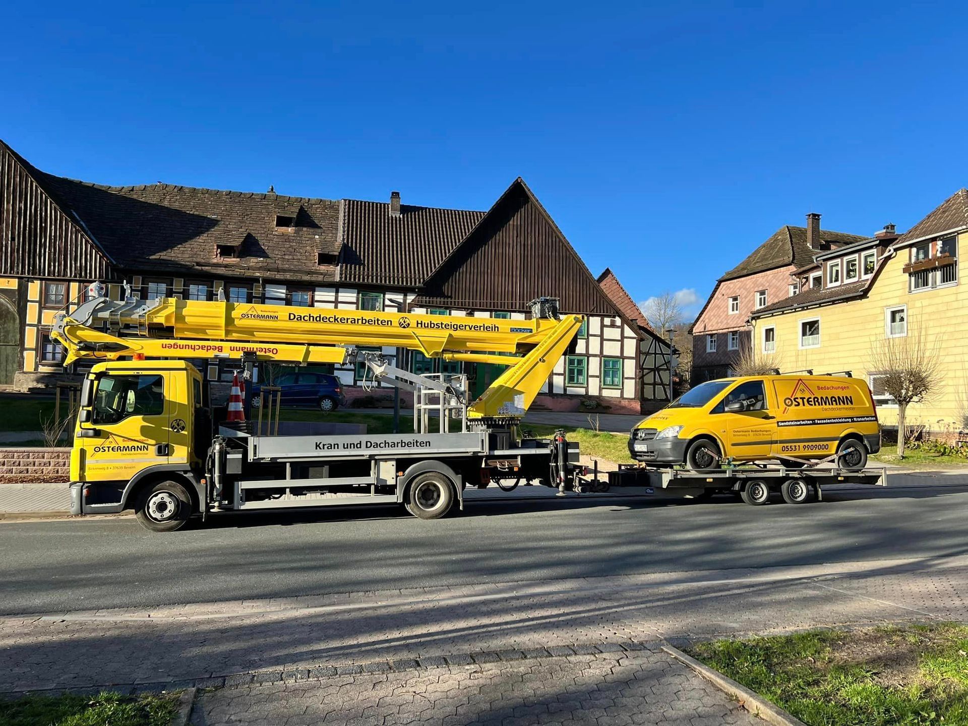 Ein gelber Lastwagen mit einem daran befestigten Kran steht am Straßenrand neben einem gelben Lieferwagen.