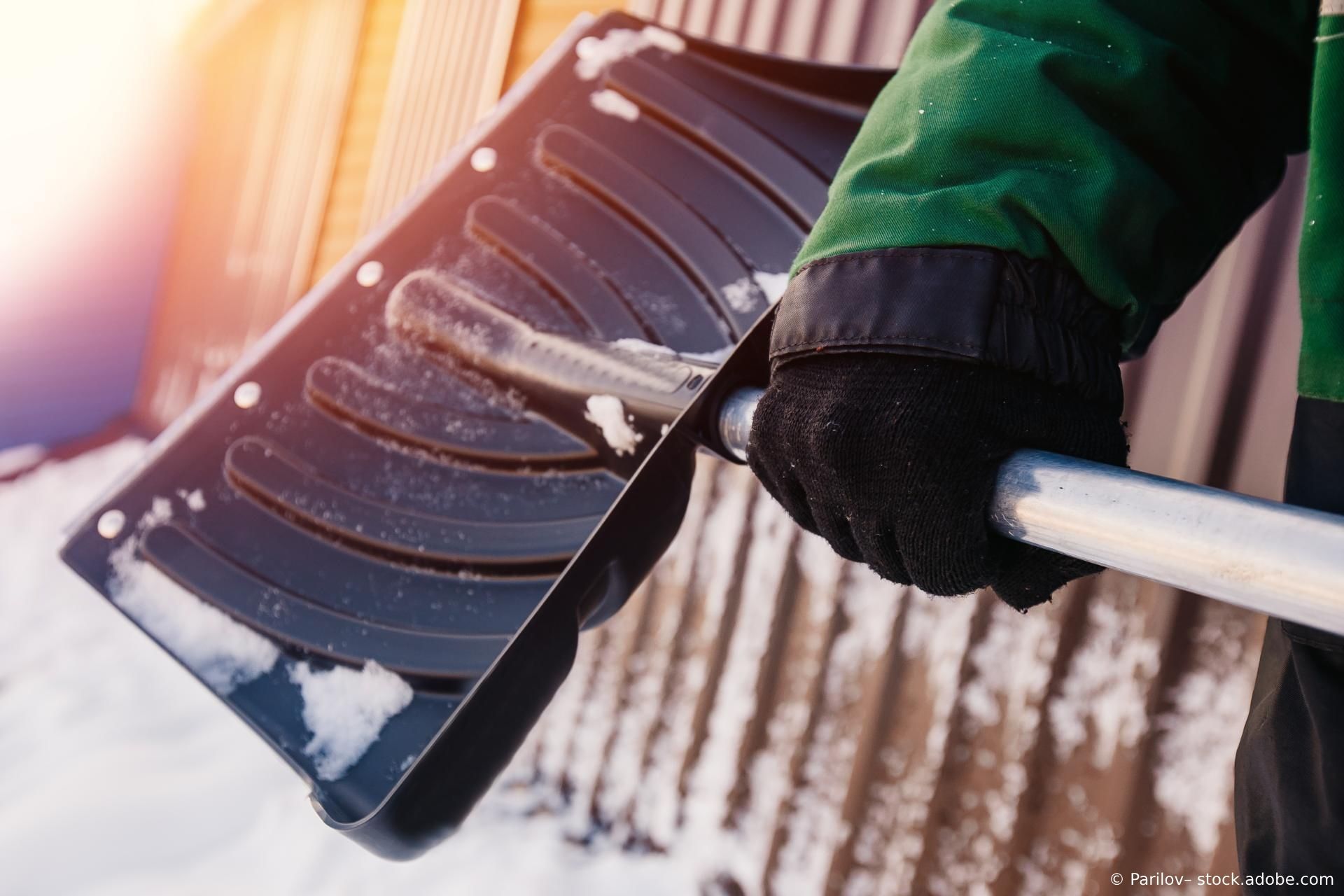 Nahaufnahme einer Schaufel zum Schneeräumen im Winter in den Händen eines Mannes.