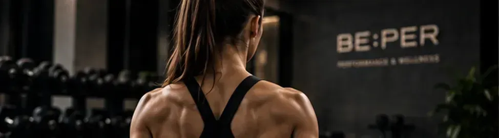 Mancuernas negras sobre un suelo oscuro de gimnasio, con más pesas borrosas al fondo.