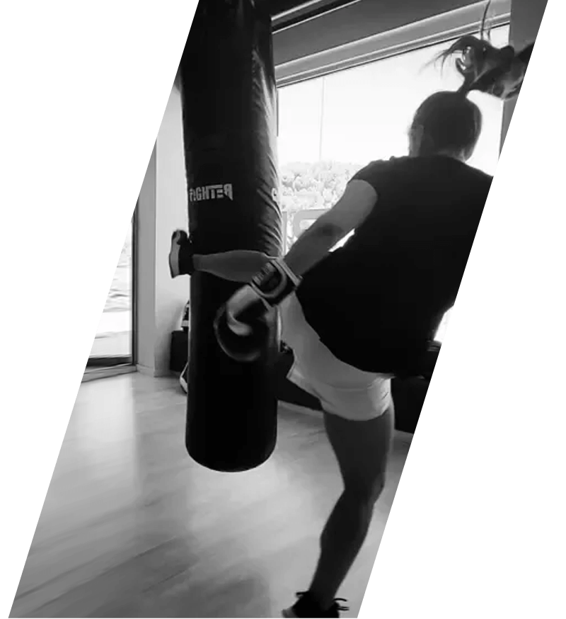 Una mujer patea un saco pesado en un gimnasio, toma en ángulo, en blanco y negro.
