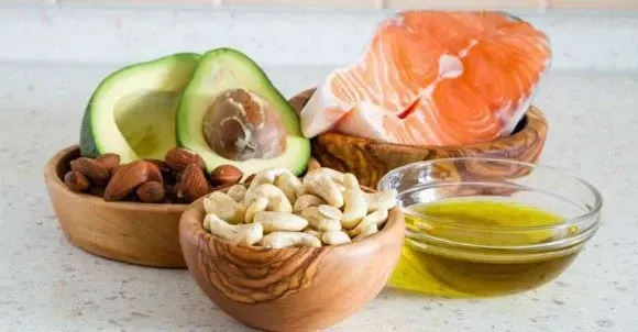 Un bol de nueces, aguacate, salmón y aceite de oliva sobre una mesa.