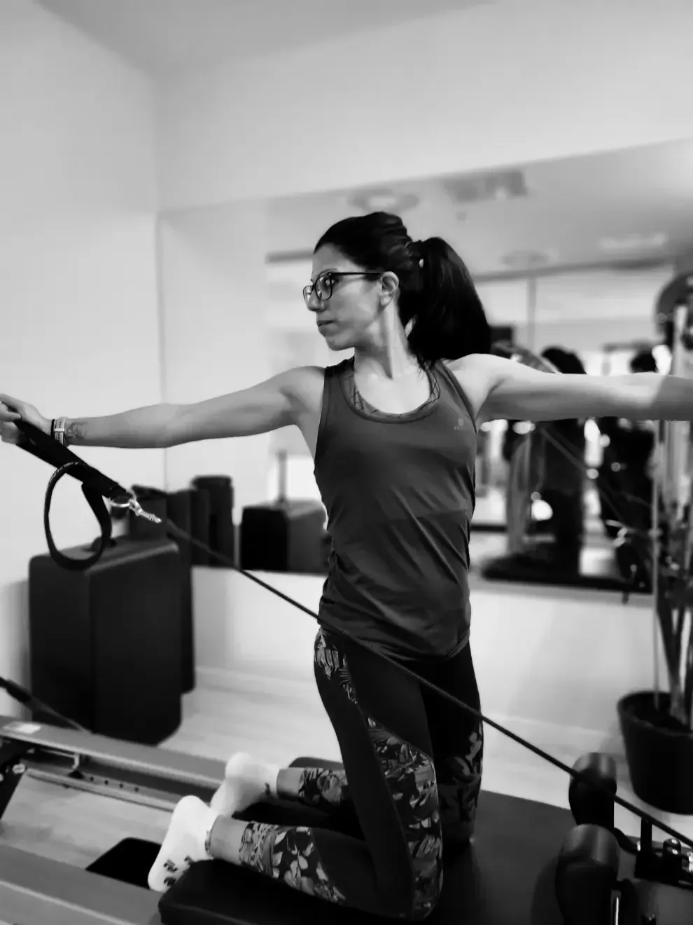 Una mujer está arrodillada en una máquina de pilates con los brazos extendidos.