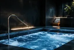 Bañera de hidromasaje interior con agua azul, pasamanos de acero inoxidable e iluminación moderna y oscura.