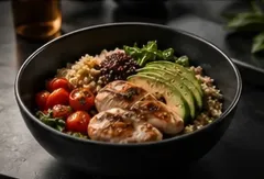 Bol de arroz con pollo a la parrilla, rodajas de aguacate, tomates cherry, verduras y salsa sobre una mesa oscura.
