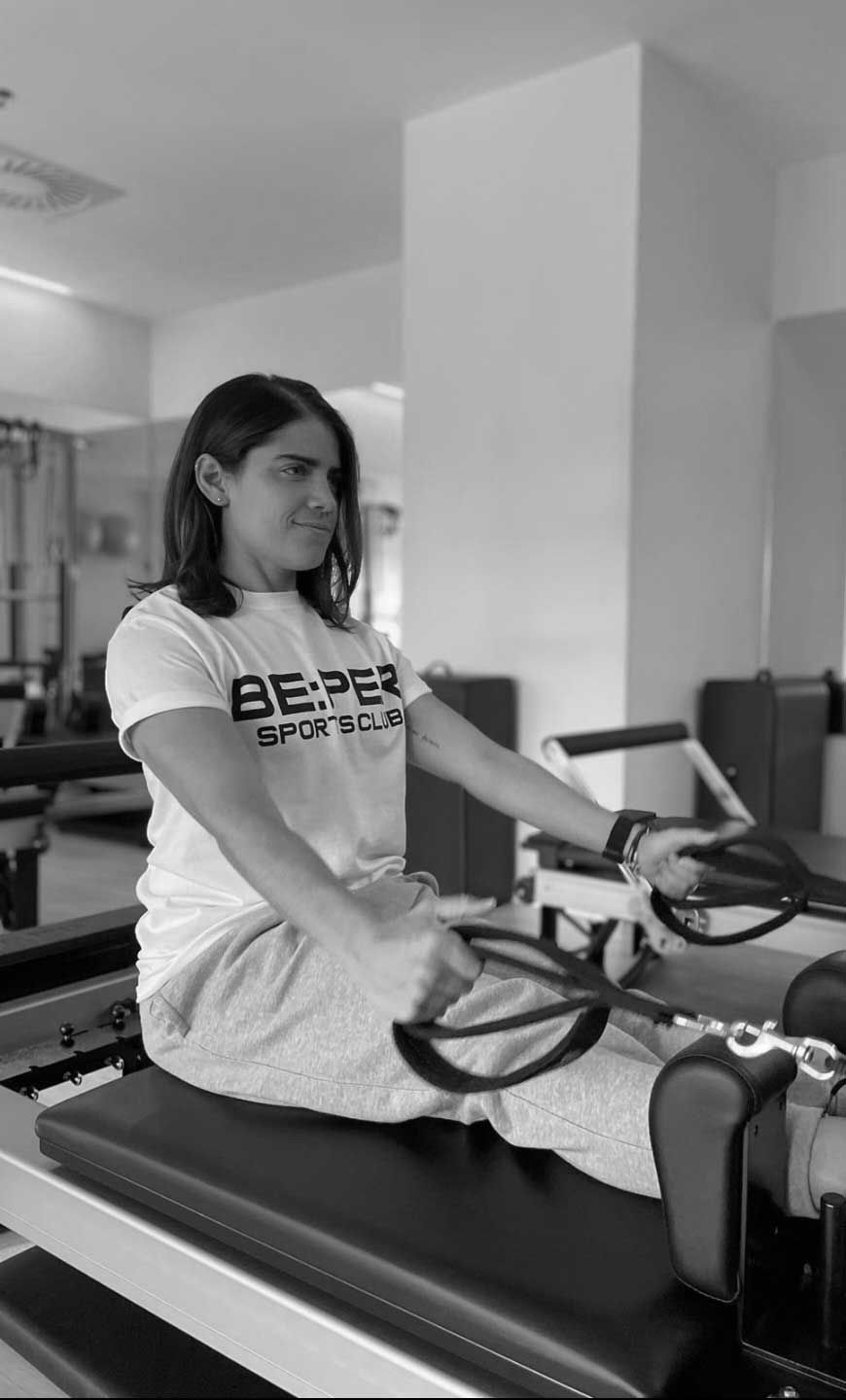 Una mujer está sentada en una máquina de pilates en un gimnasio.