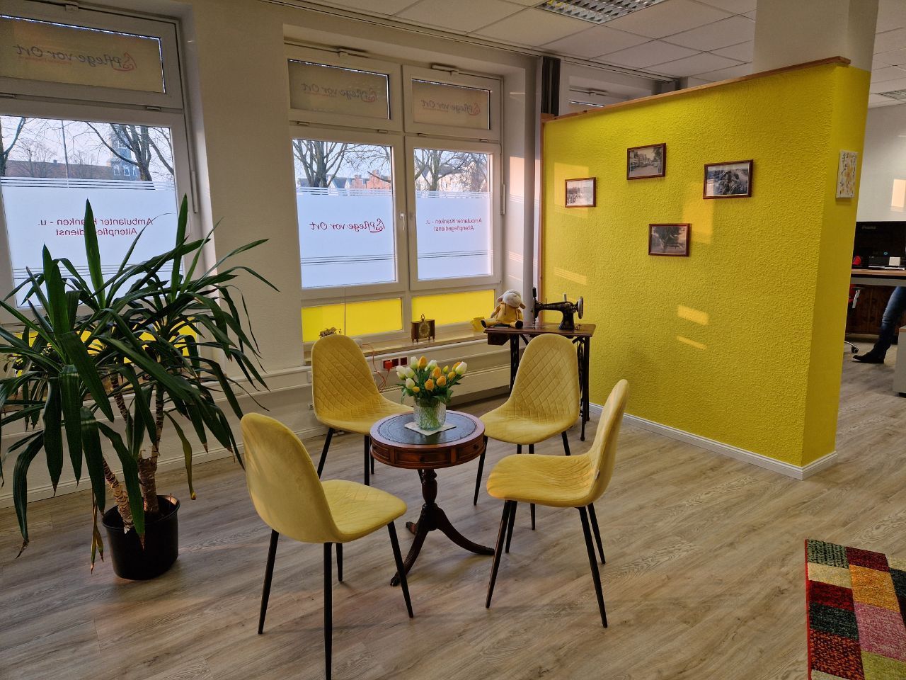 Gemütliche Lounge mit gelben Stühlen, kleinem Tisch, Pflanzen und einer leuchtend gelben Akzentwand an den großen Fenstern.