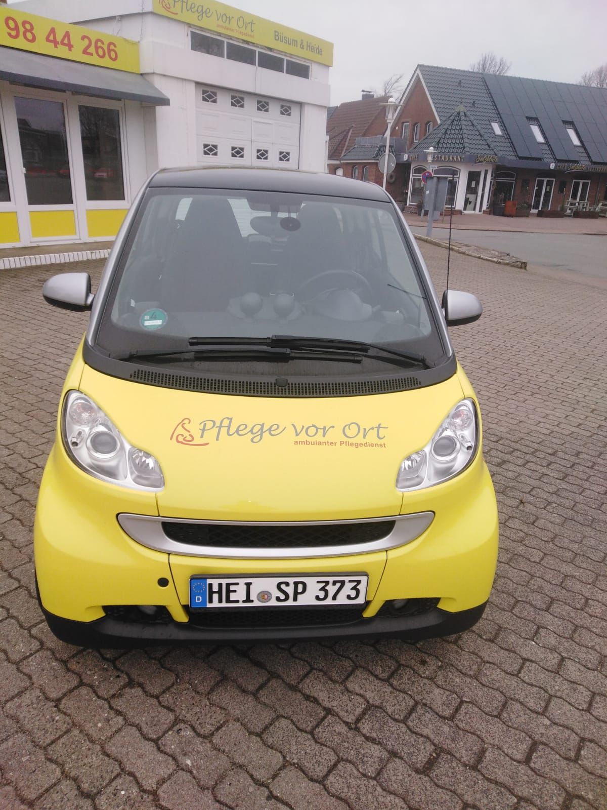 Ein gelber Smart parkt auf Kopfsteinpflaster vor einem Gebäude; auf der Motorhaube steht „Always on tour“.