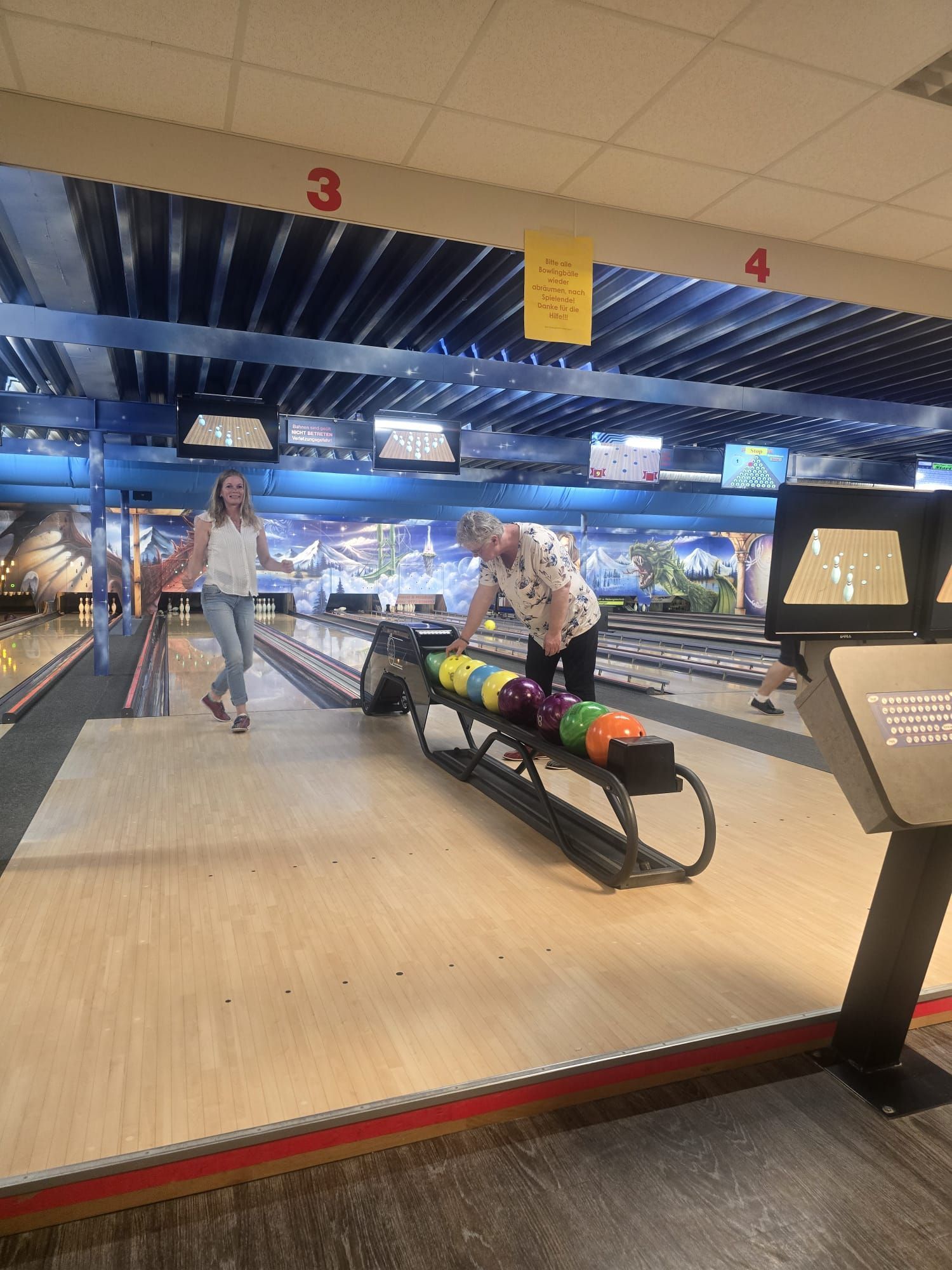 Bowlingbahn mit zwei Personen und bunten Kugeln in der Nähe der Kugelrückgabe.