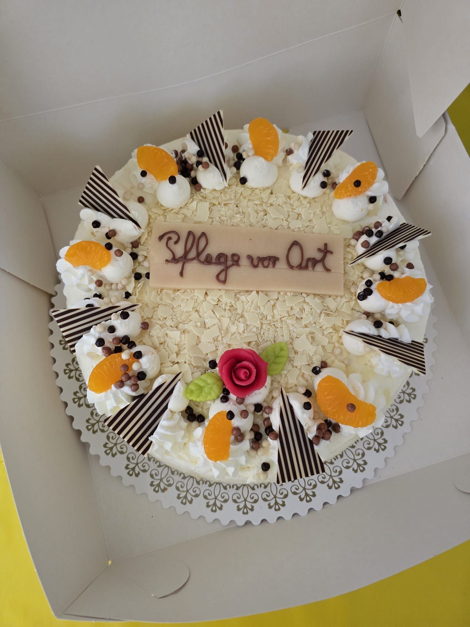 Runder weißer Kuchen mit Schokoladen- und Orangenverzierungen und der Aufschrift „Pflege vor Ort“ in der Mitte.