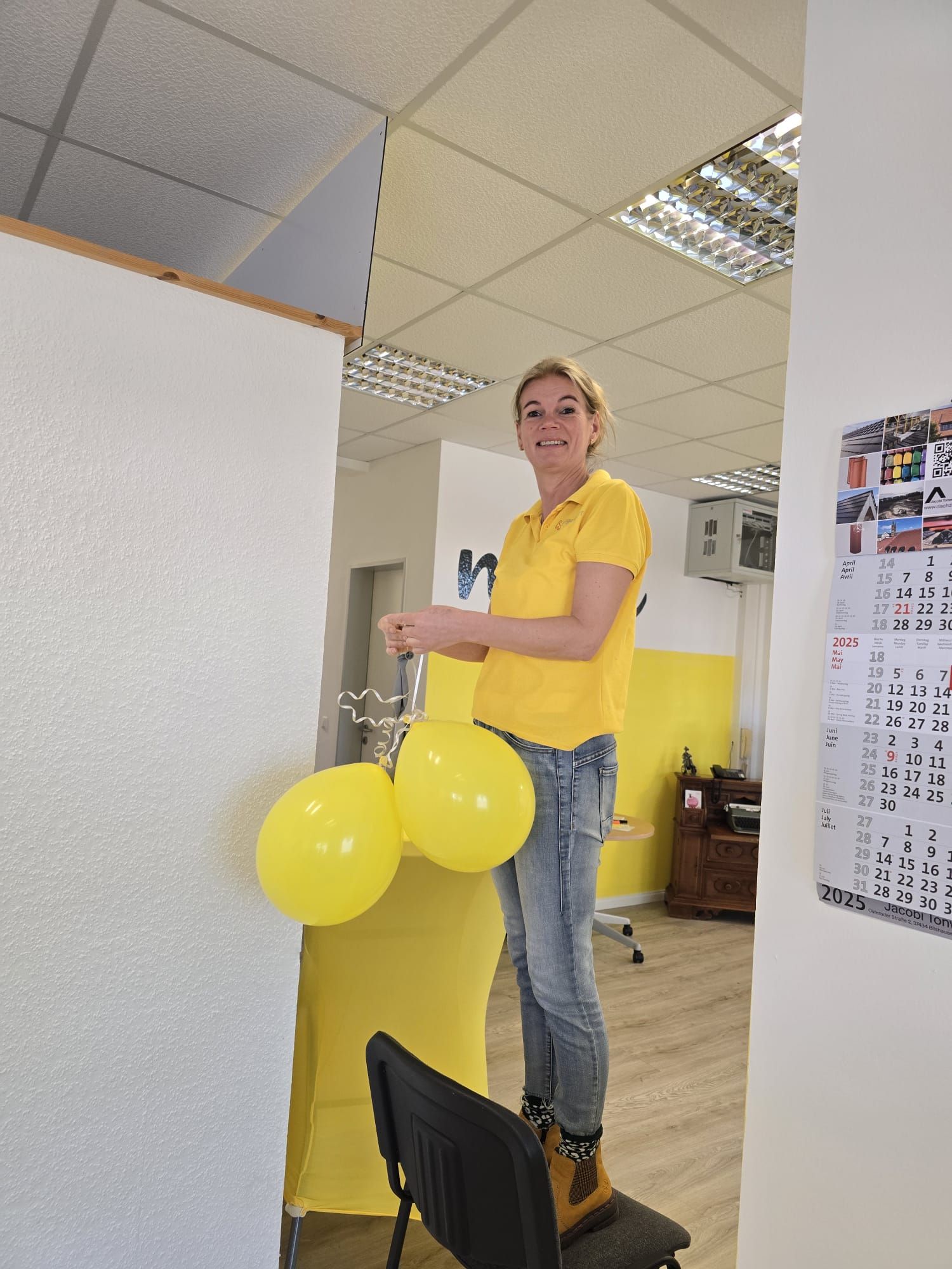 Eine Person in einem gelben Hemd hält gelbe Luftballons in einem Büroflur.