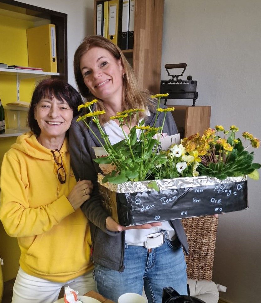 Zwei lächelnde Personen halten einen mit Blumen gefüllten Korb in einem Innenraum.