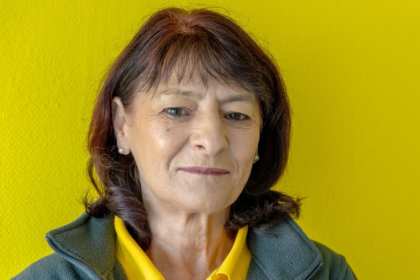 Porträt einer Frau in gelbem Oberteil und grüner Jacke vor leuchtend gelbem Hintergrund