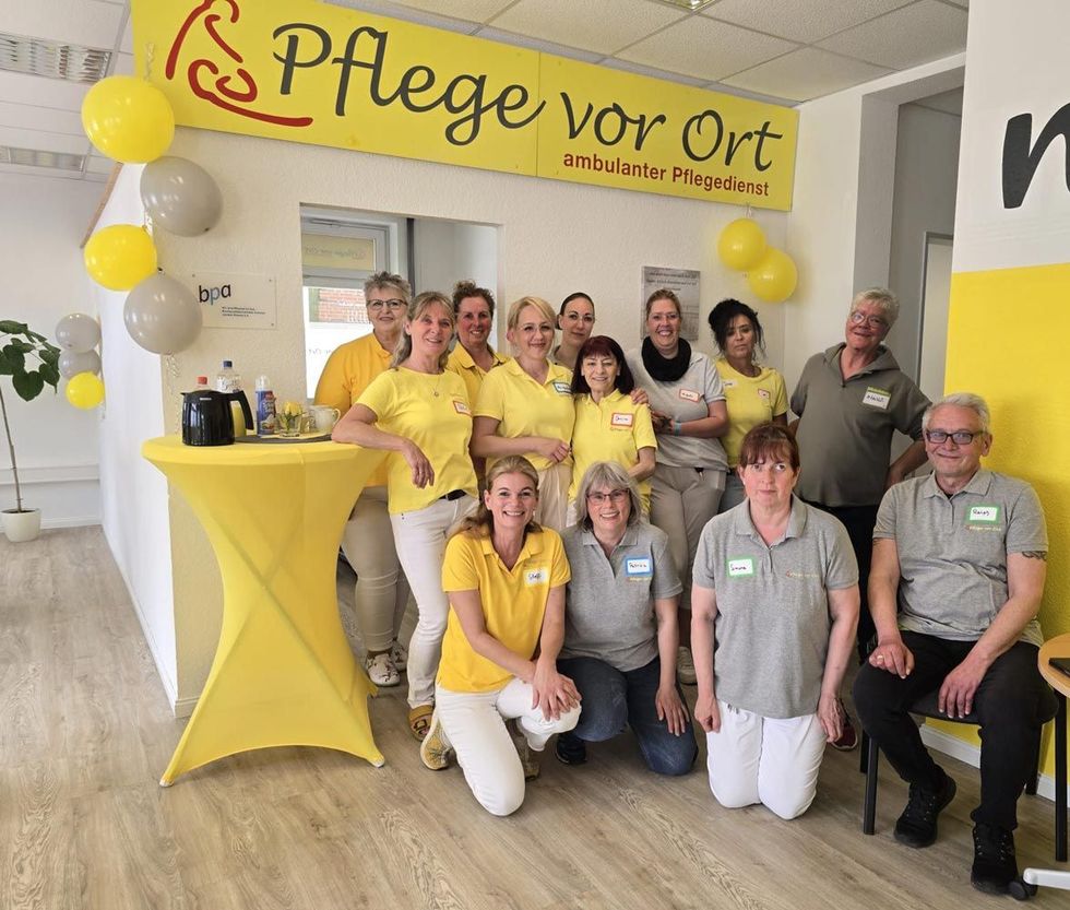 Eine Gruppe von Menschen in Gelb an einem Stand der Pflege vor Ort mit Luftballons und einem Banner