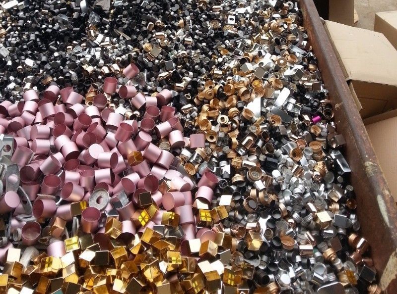 Un contenedor lleno de una colección desorganizada de piezas metálicas cilíndricas y rectangulares de color rosa, dorado, plateado y negro.