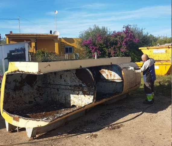 Un trabajador rocía con pintura un gran tanque metálico de color crema, que ha sido abierto por la mitad, al aire libre en un día soleado.