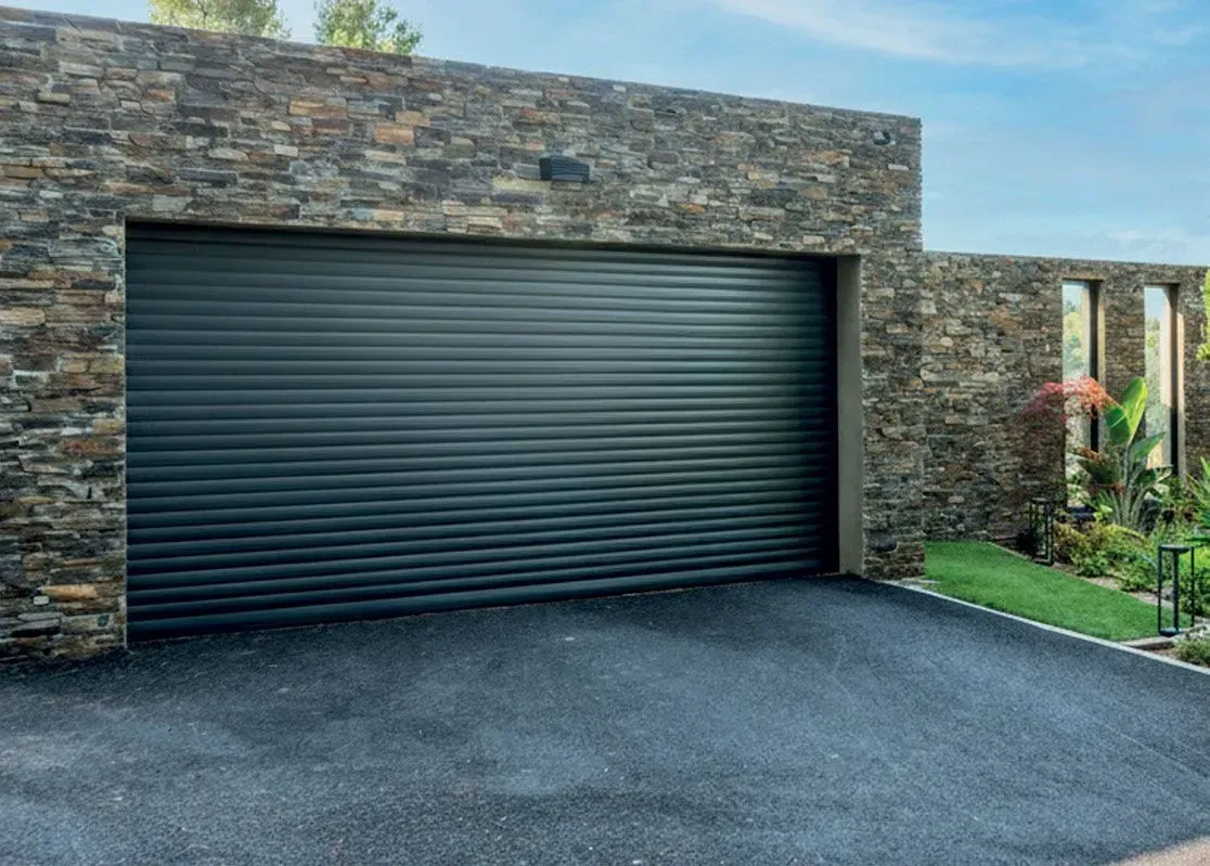 Garage en pierre avec porte sectionnelle sombre fermée et allée pavée.