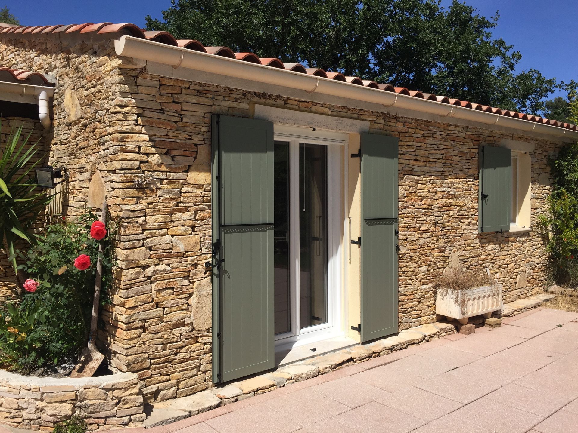 Façade d'une maison en pierre avec des volets vert.