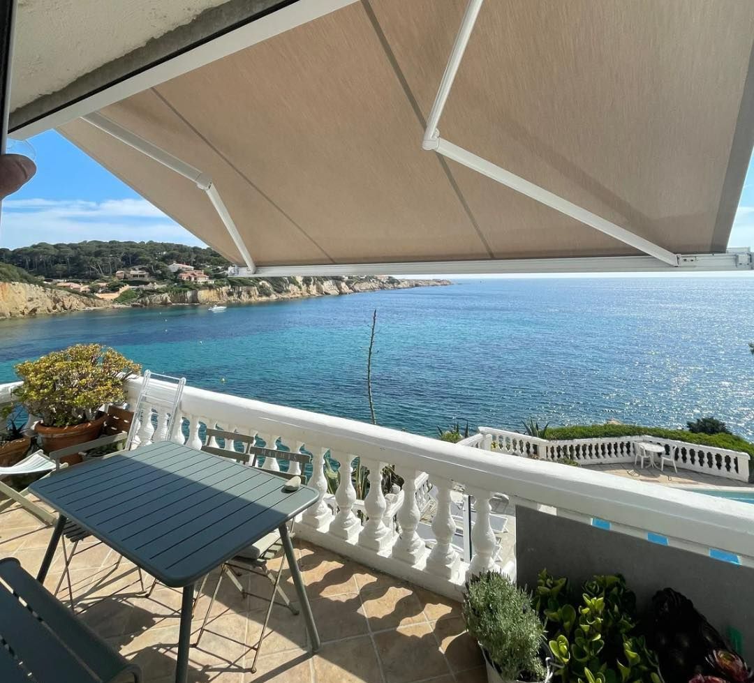 Store banne beige sur une terrasse donnant sur la mer.