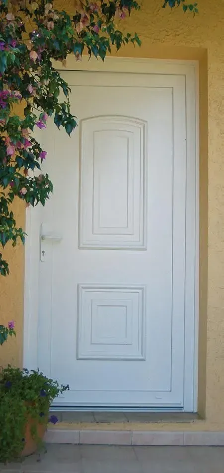 Porte d'entrée à panneaux blancs encadrée de stuc crème et de vignes vertes grimpantes