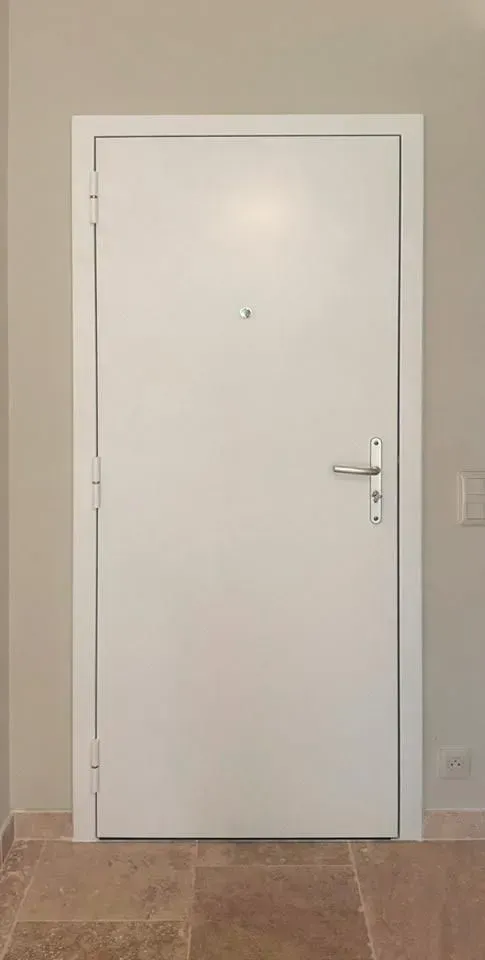 Porte intérieure blanche avec poignée argentée dans un couloir beige, encadrée par un sol carrelé.