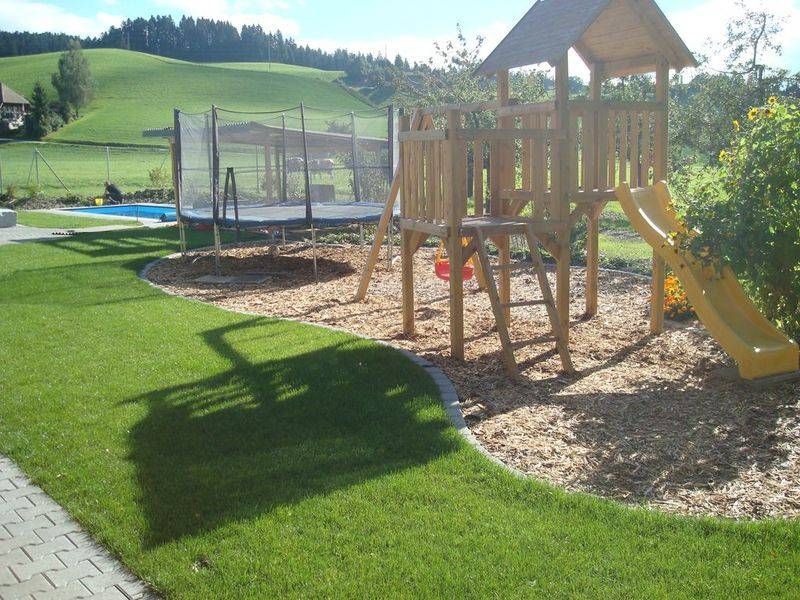 Ein Holzspielplatz mit Rutsche und Trampolin. Foto von der Schöni Blumen und Gartenbau GmbH