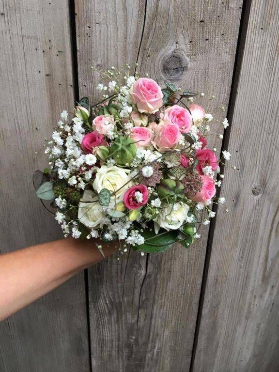 Eine Person hält einen Strauß rosa und weißer Blumen vor einer Holzwand.
