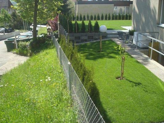 Ein Maschendrahtzaun umgibt einen üppigen grünen Rasen vor einem Haus.