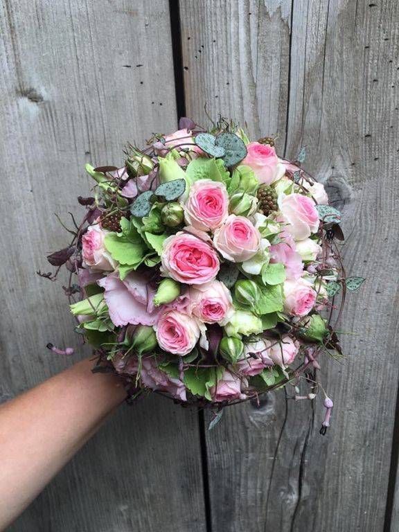 Eine Person hält einen Strauss rosa Rosen vor einer Holzwand. Foto von der Schöni Blumen und Gartenbau GmbH