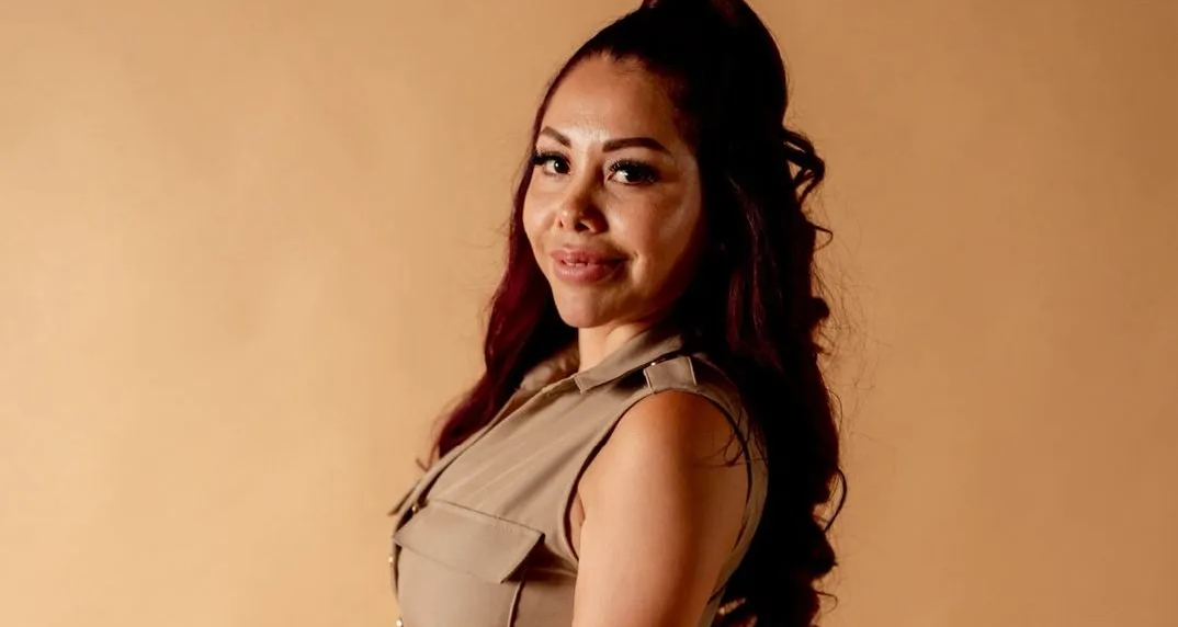 Una persona con cabello largo y oscuro que viste una camisa beige