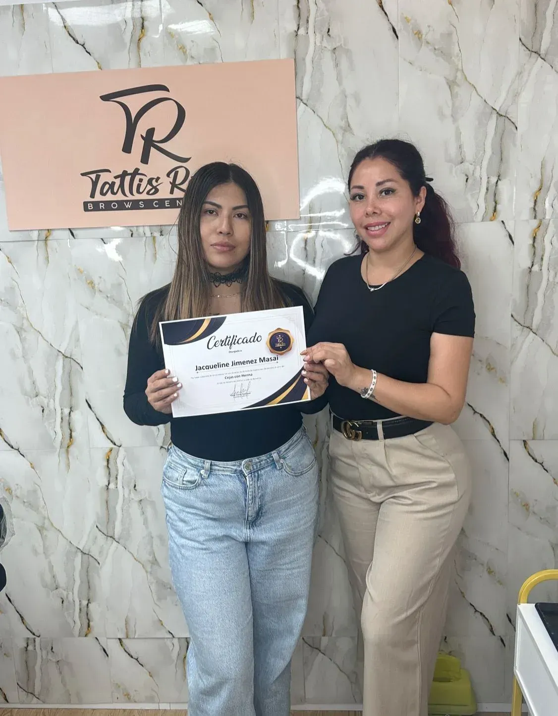 Dos personas posan frente al logotipo de Tattis R; una de ellas sostiene un certificado en un entorno profesional.