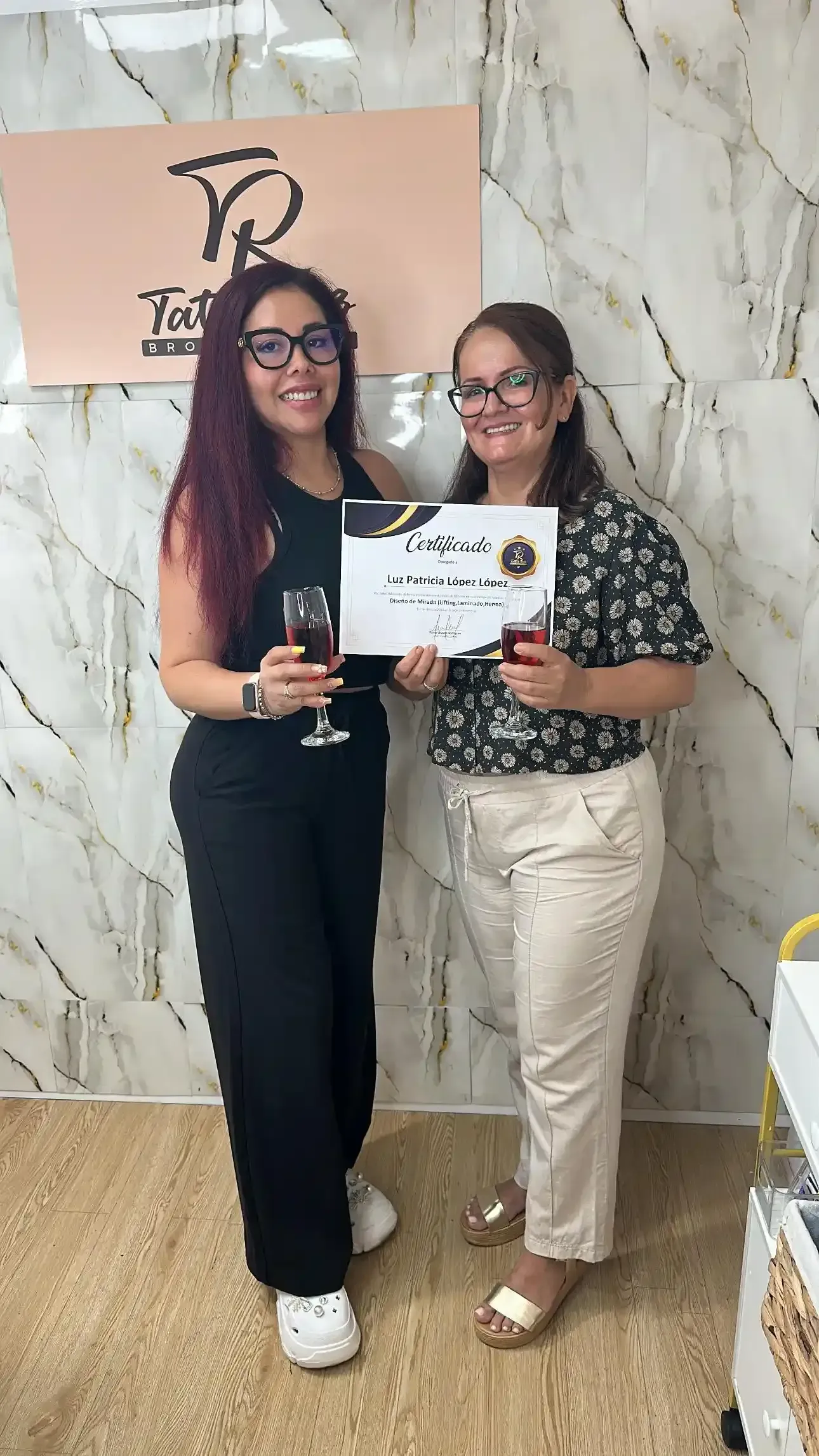Dos personas de pie en un estudio con un fondo de mármol, sosteniendo un certificado