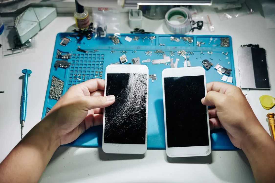 Manos sosteniendo dos teléfonos inteligentes blancos, uno de ellos con la pantalla rota