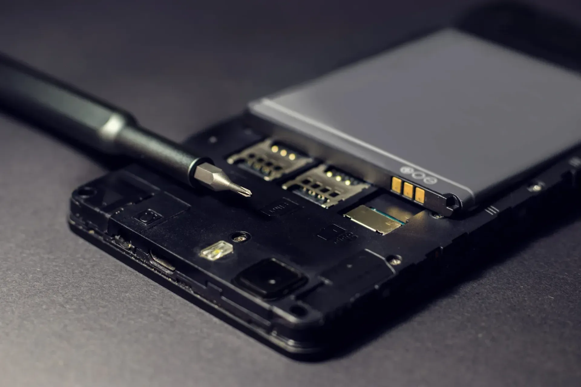 Celular en reparacion, destornillador al lado de la bateria y ranuras para tarjeta SIM.