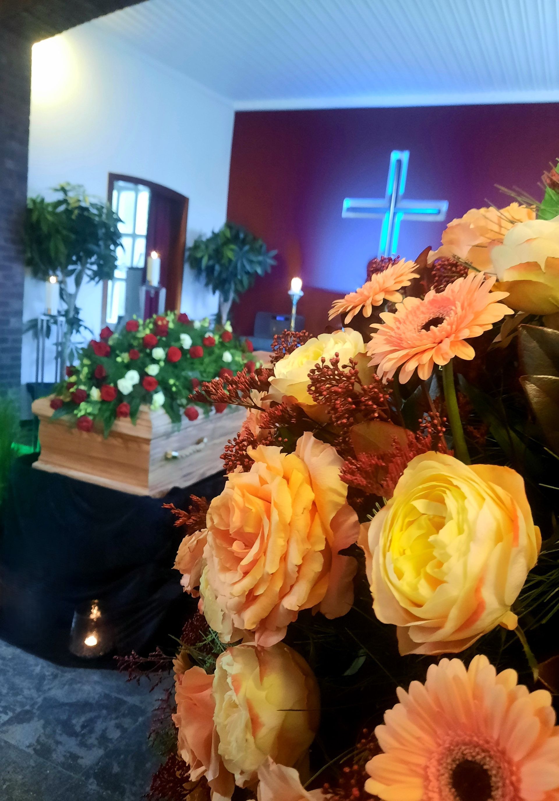 Ein Sarg ist von Blumen umgeben in einer Kirche mit einem Kreuz im Hintergrund