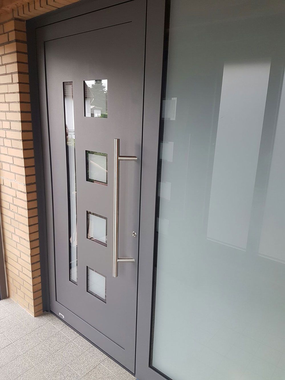 Eine graue Tür mit quadratischen Fenstern und einem Edelstahlgriff