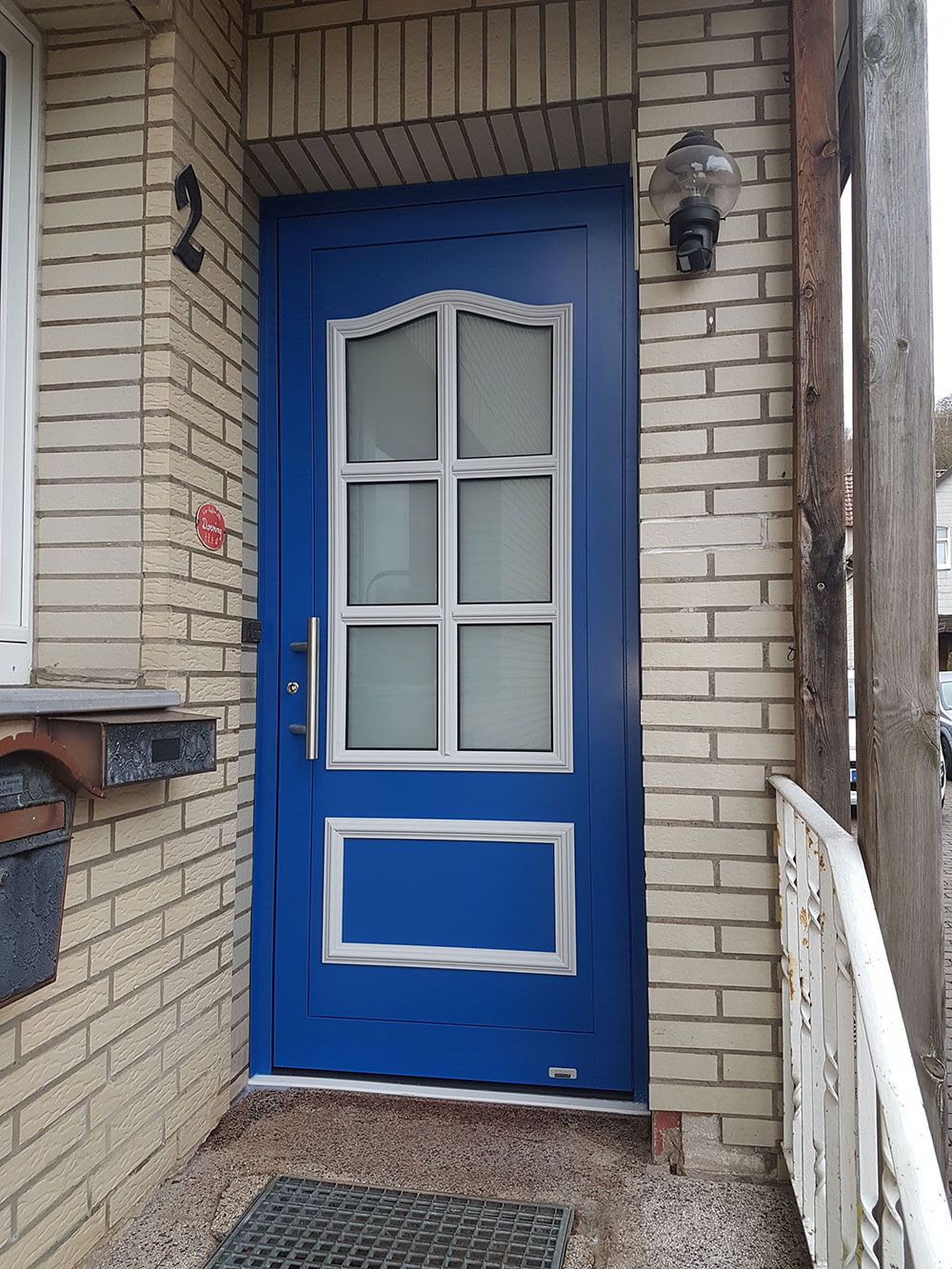 An einem weißen Backsteingebäude befindet sich eine blaue Tür mit weißen Verzierungen.