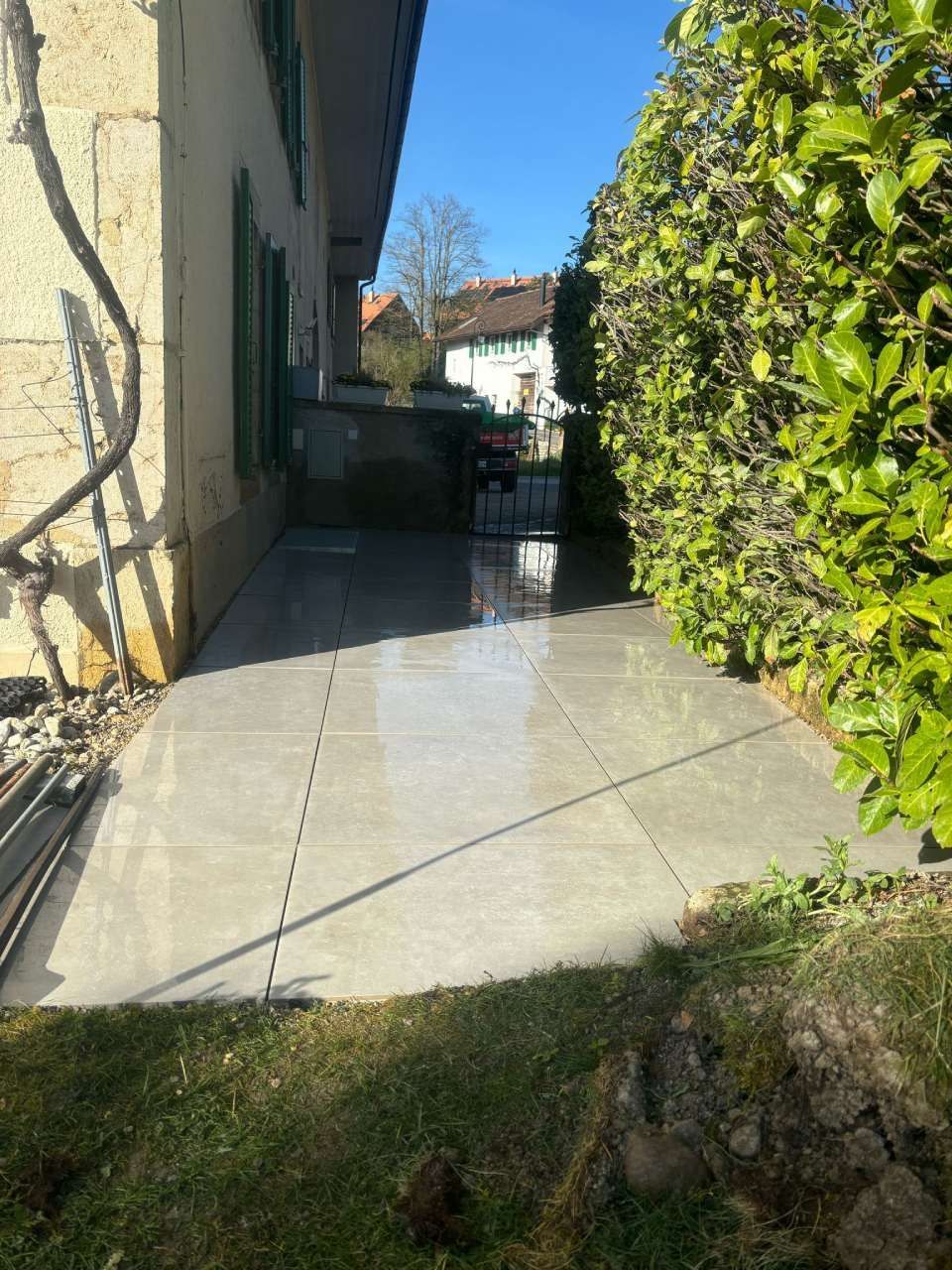 Une allée en béton menant à une maison avec une haie en arrière-plan.