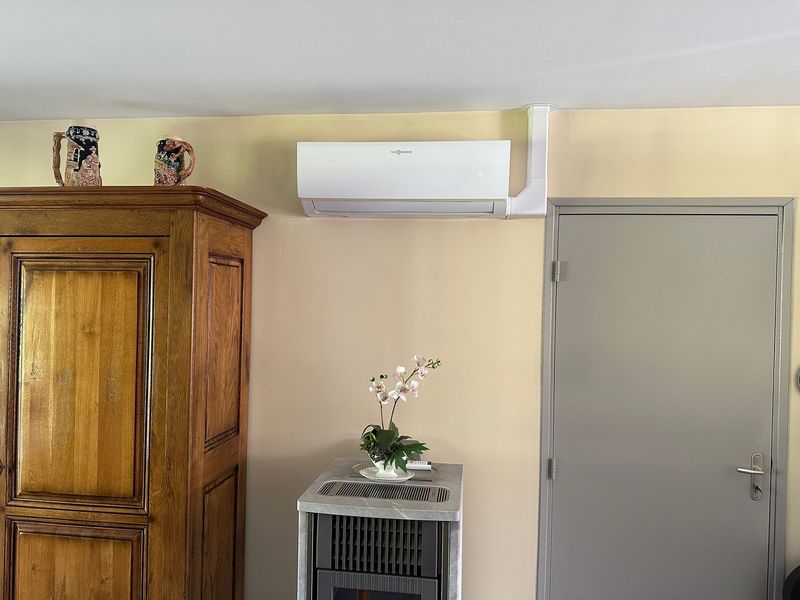 Un climatiseur est installé au-dessus d'une petite table et d'une armoire en bois, à côté d'une porte grise.