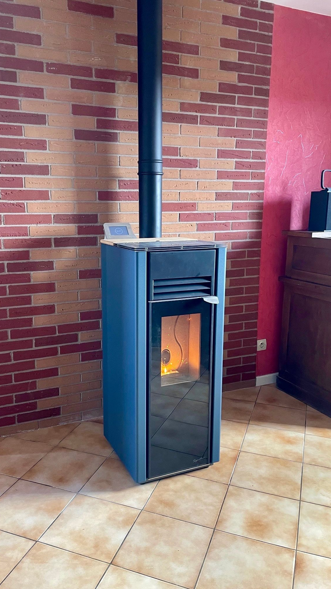 Poêle à granulés rouge avec conduit noir, allumé et en fonctionnement.