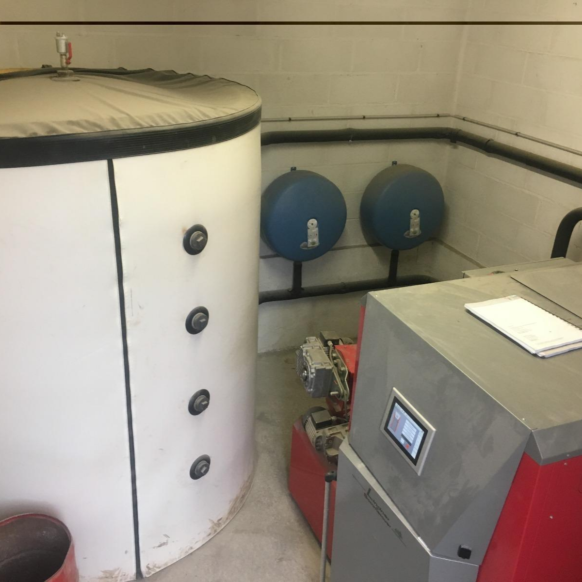 Installation intérieure avec ballon de stockage et chaudière, reliés par des tuyaux et deux vases d’expansion muraux.
