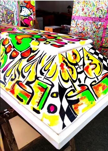 Bunte, abstrakte Kunst, gemalt auf der Oberseite einer weißen Holzkiste, möglicherweise einem Sarg.
