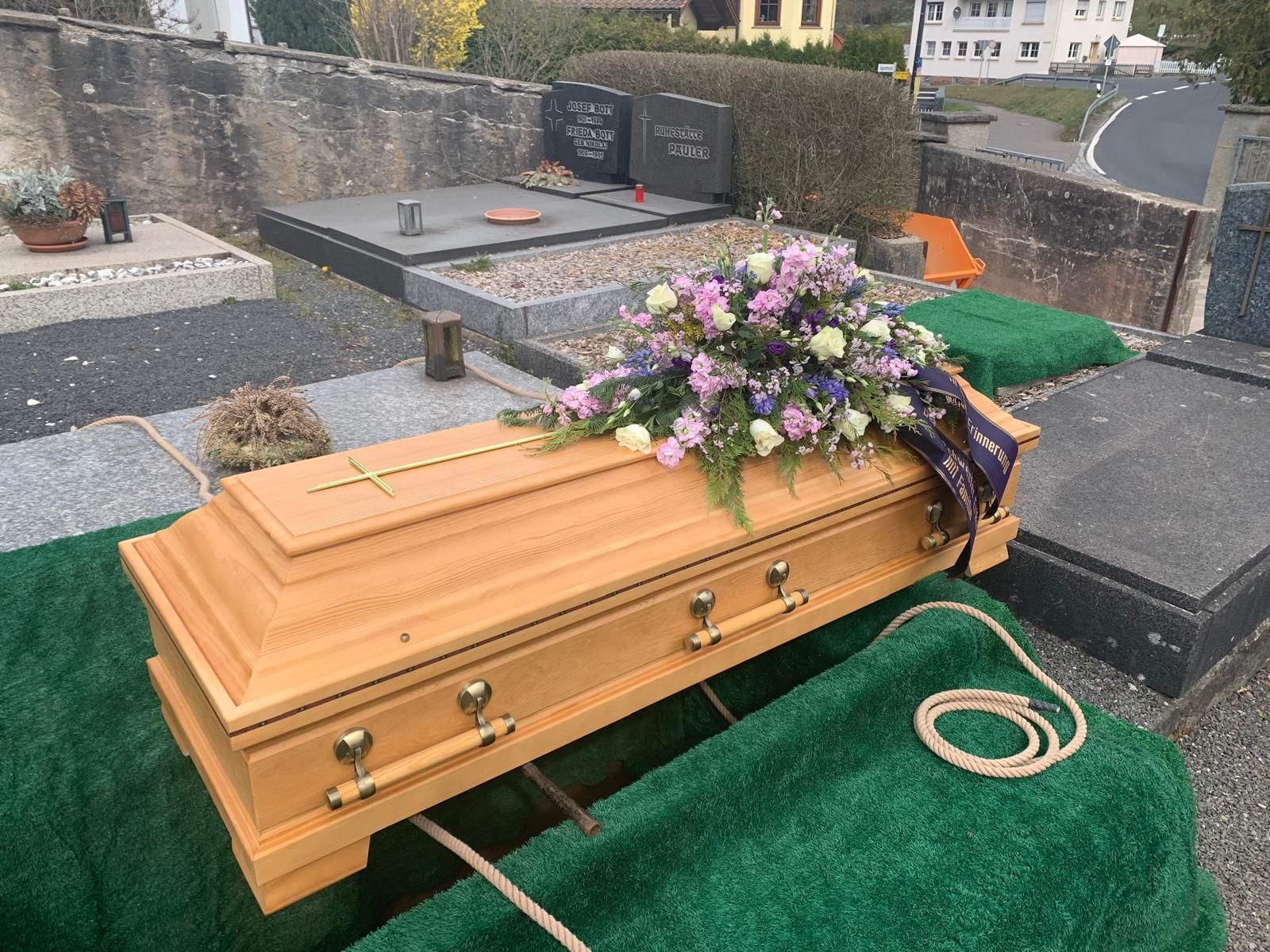 Ein Holzsarg mit Blumen auf einem Friedhof.